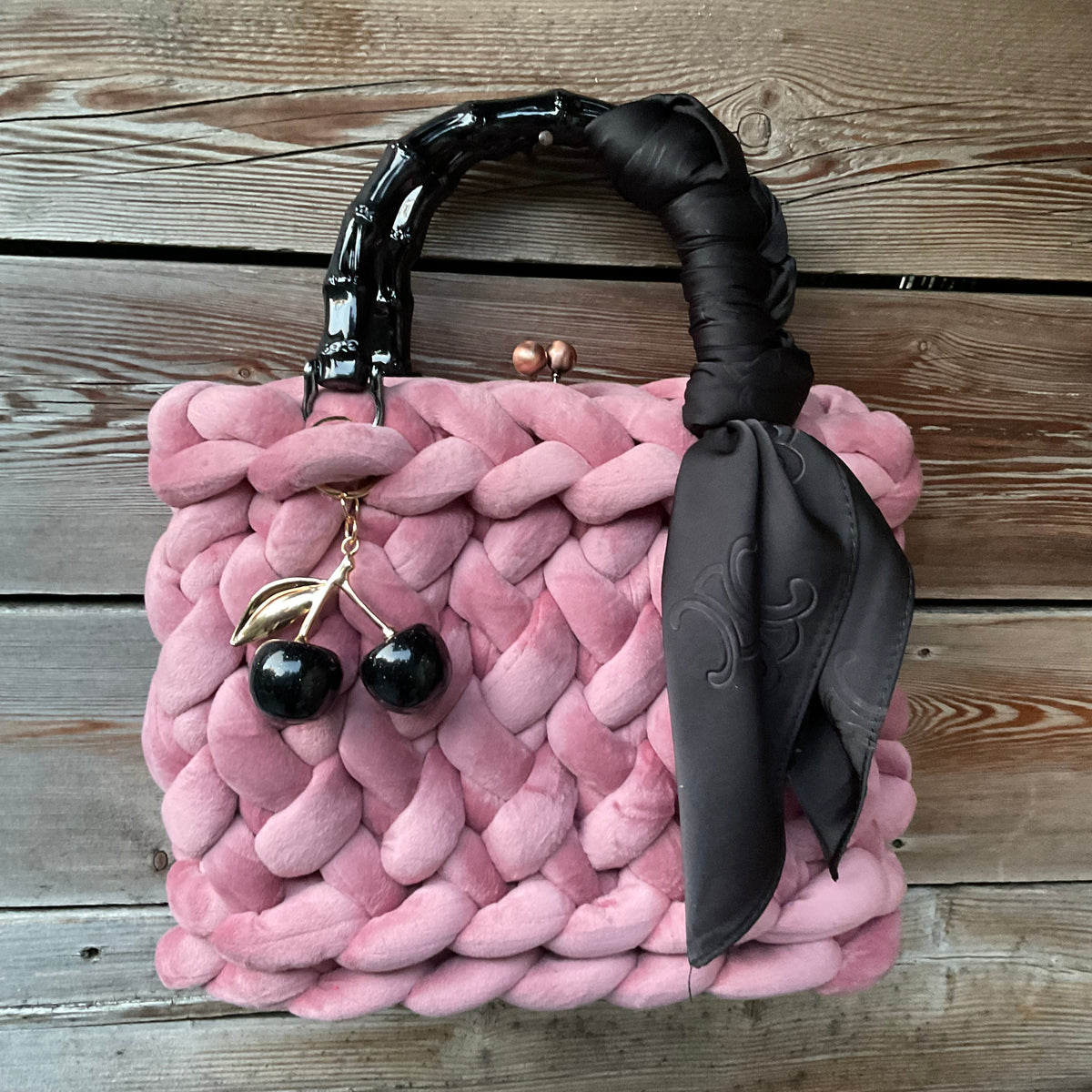 Eine gestrickte rosafarbene Trachtentasche mit Kirschanhänger und Bambusgriffen 