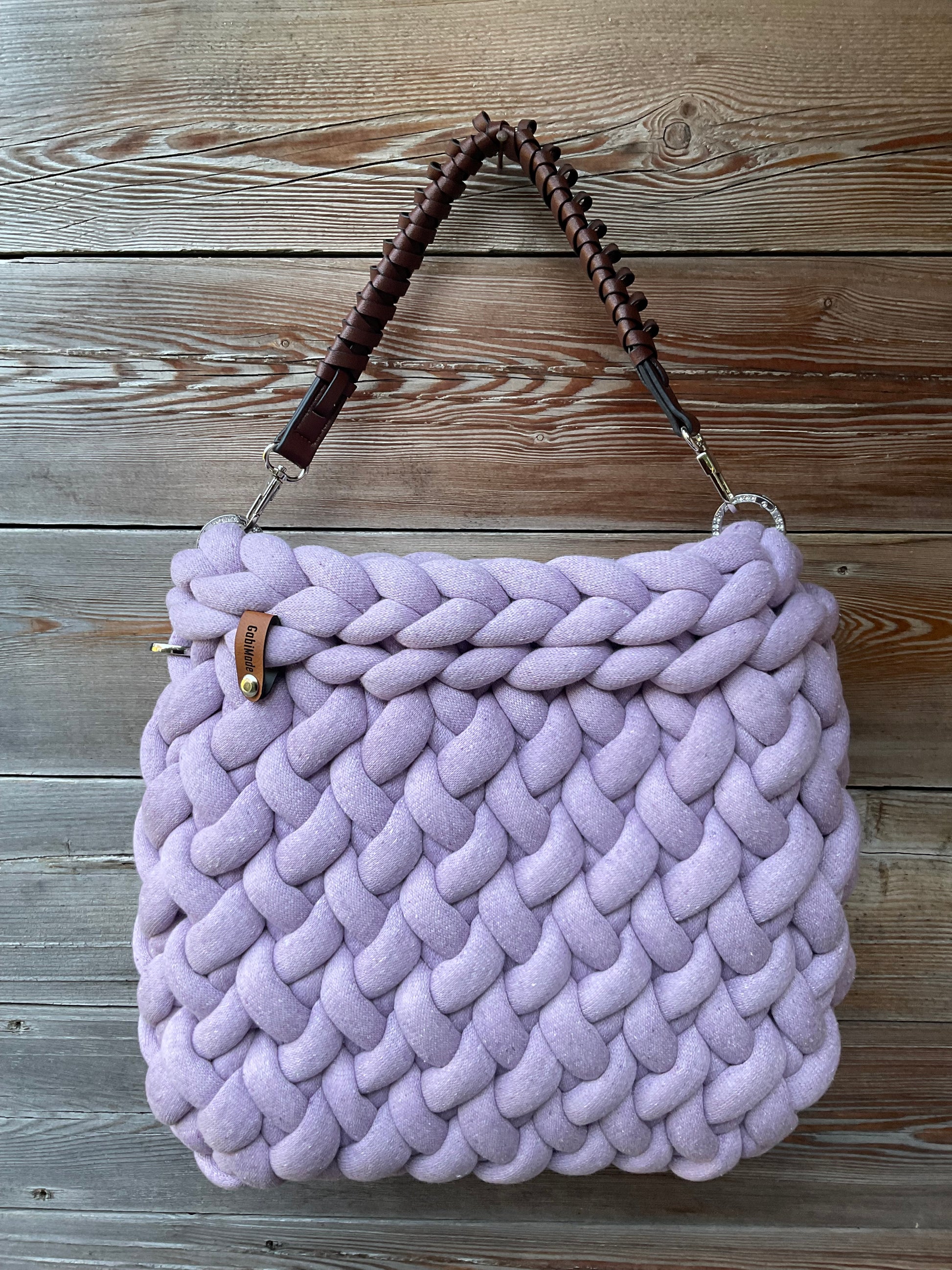 Eine gestrickte fliederfarbene Tasche mit braunen Henkel 