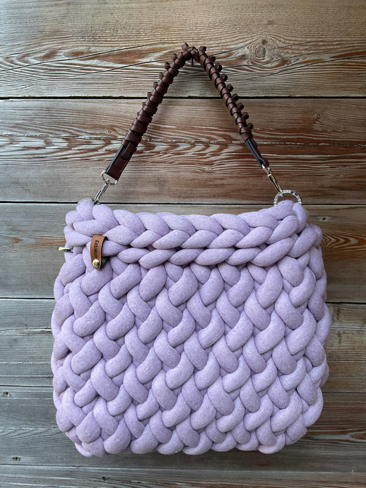 Eine gestrickte fliederfarbene Tasche mit braunen Henkel 