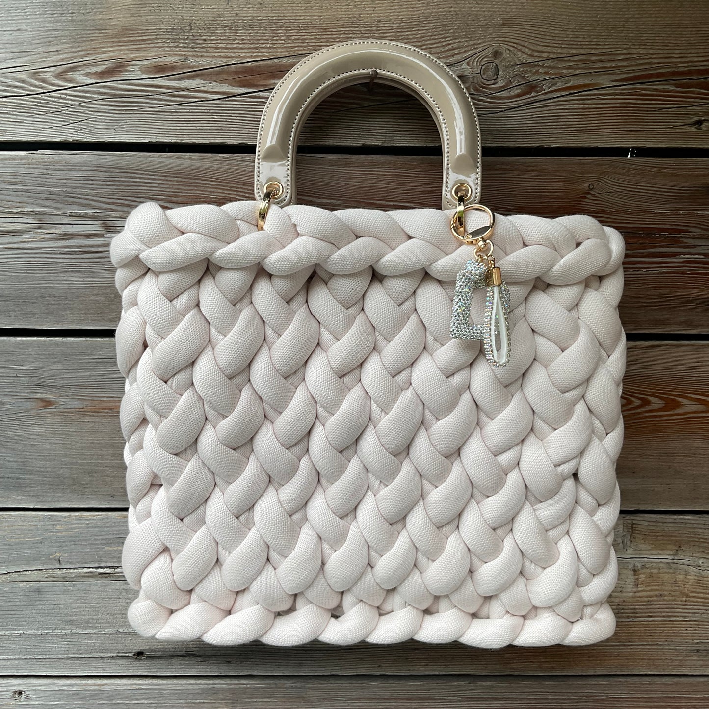 Eine cremefarbene gestrickte Tasche mit Anhänger und Henkel 