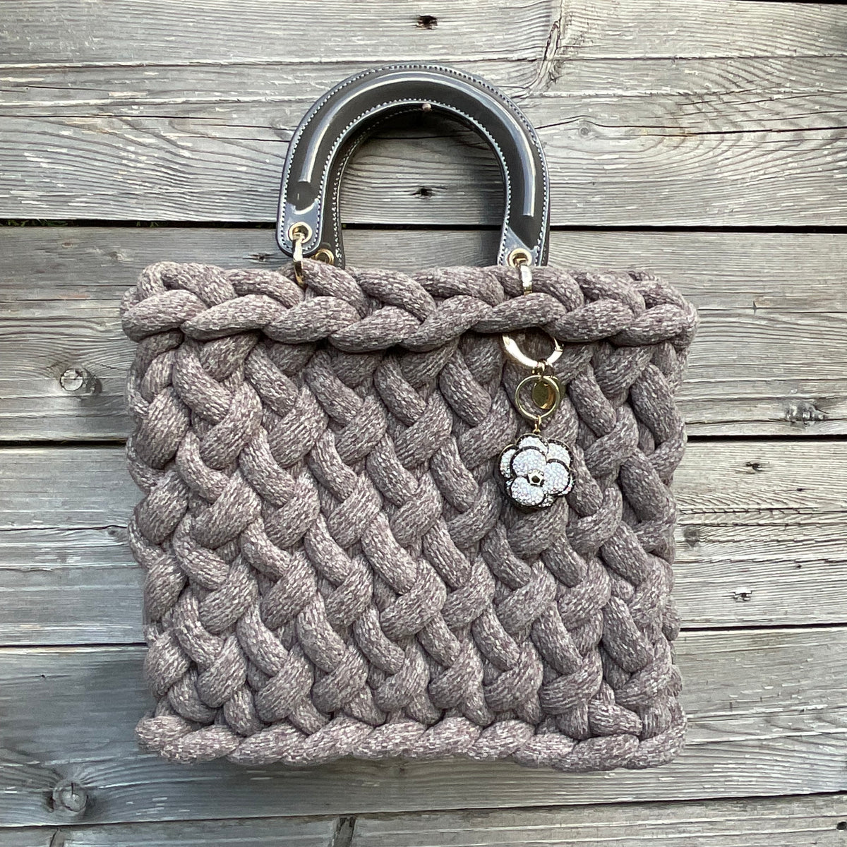 Eine gestrickte graue Tasche mit Anhänger und Lackgriffen