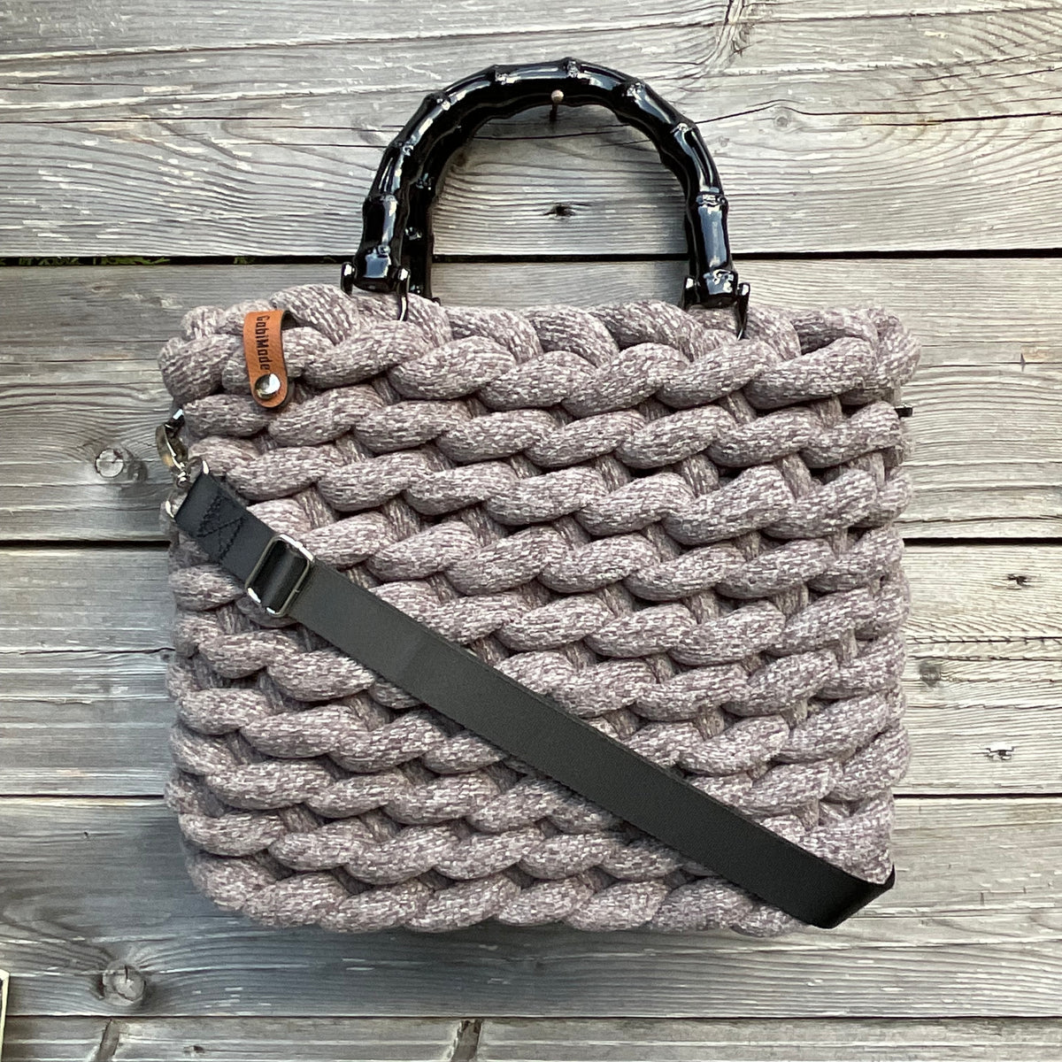 Eine graue gestrickte Tasche mit Bambusgriffen und Gurt 