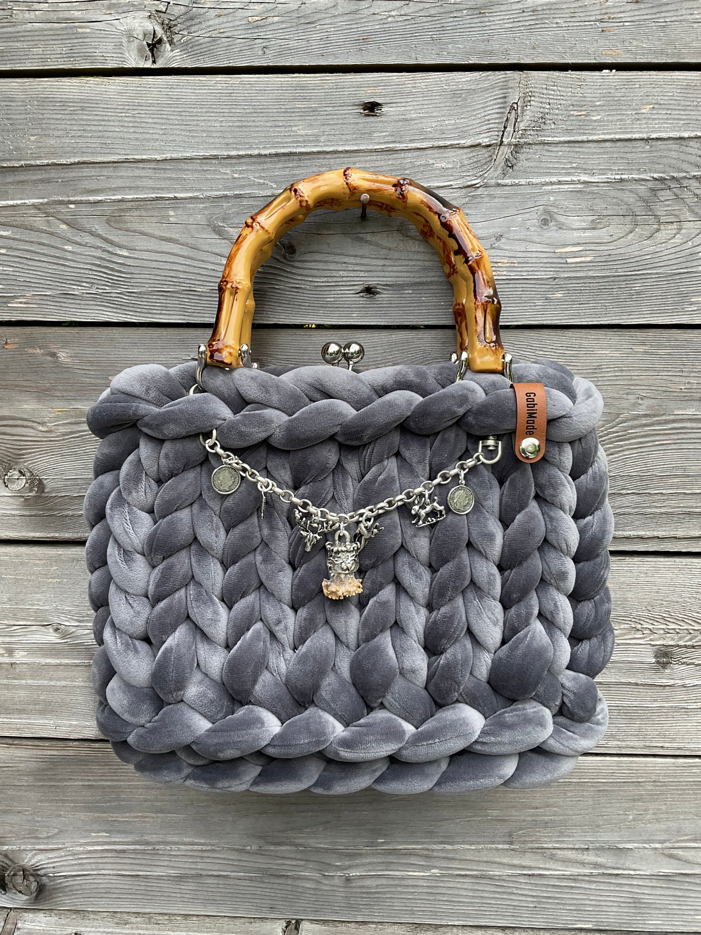 Eine graue gerstrickte Trachtentasche mit Bambusgriffen und einem Carivari.