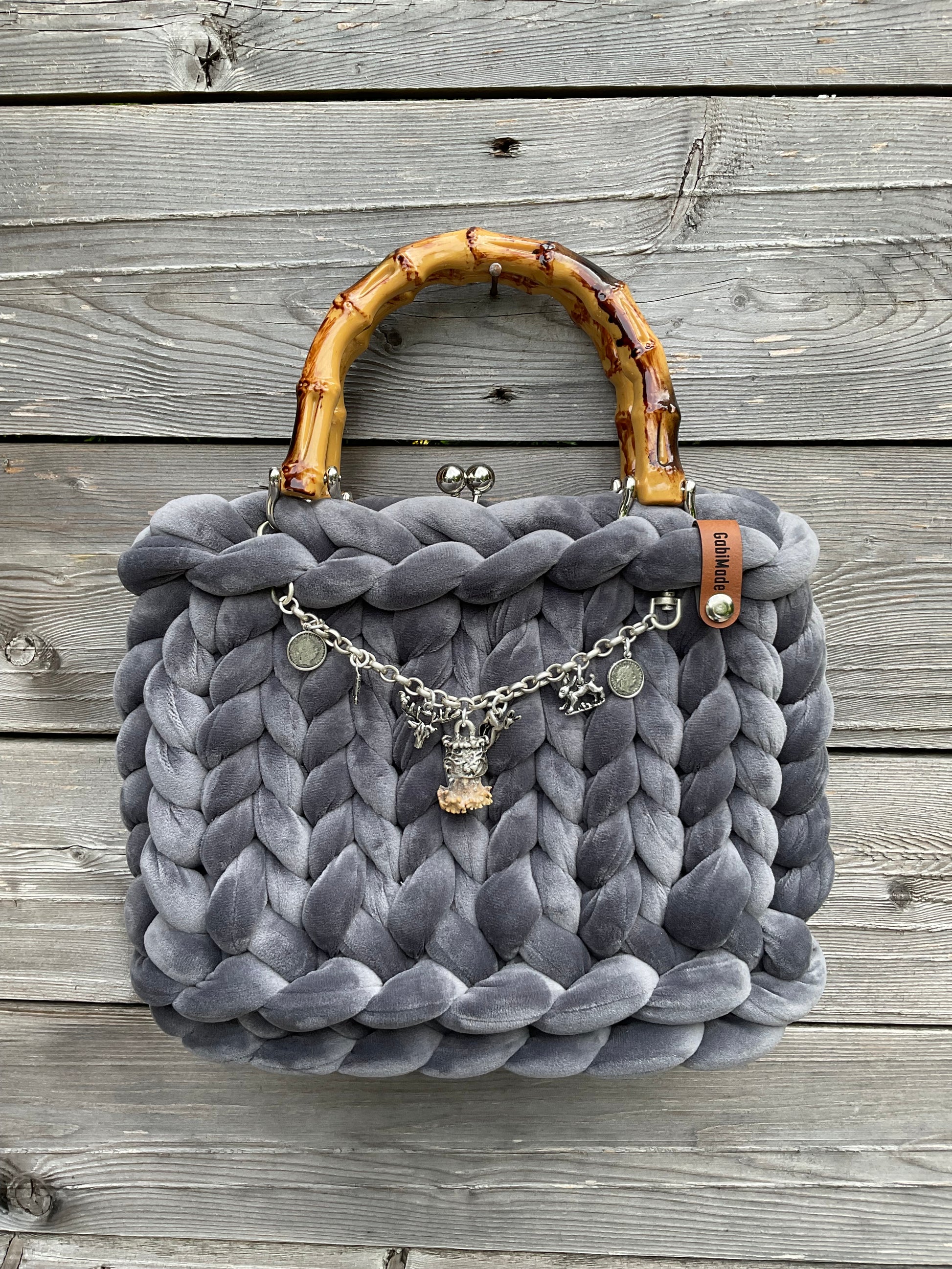 Eine graue gerstrickte Trachtentasche mit Bambusgriffen und einem Carivari.