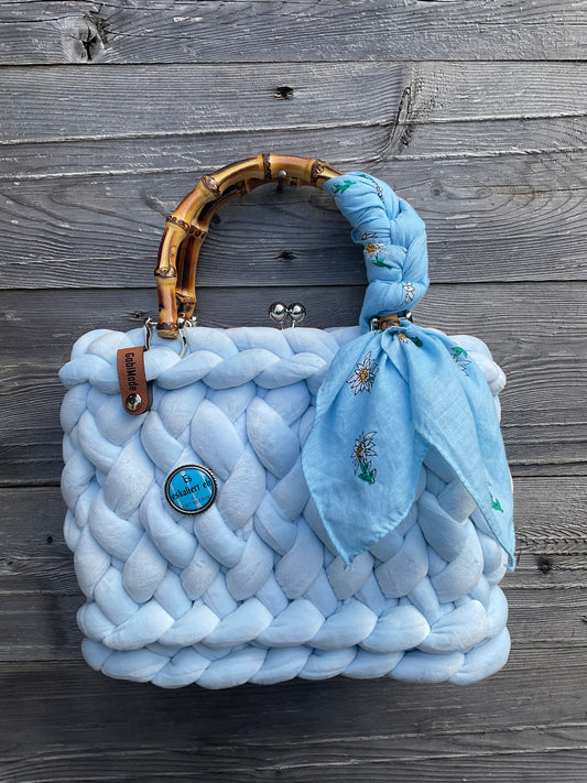 Eine gestrickte hellblaue Tasche mit Tuch und Brosche 