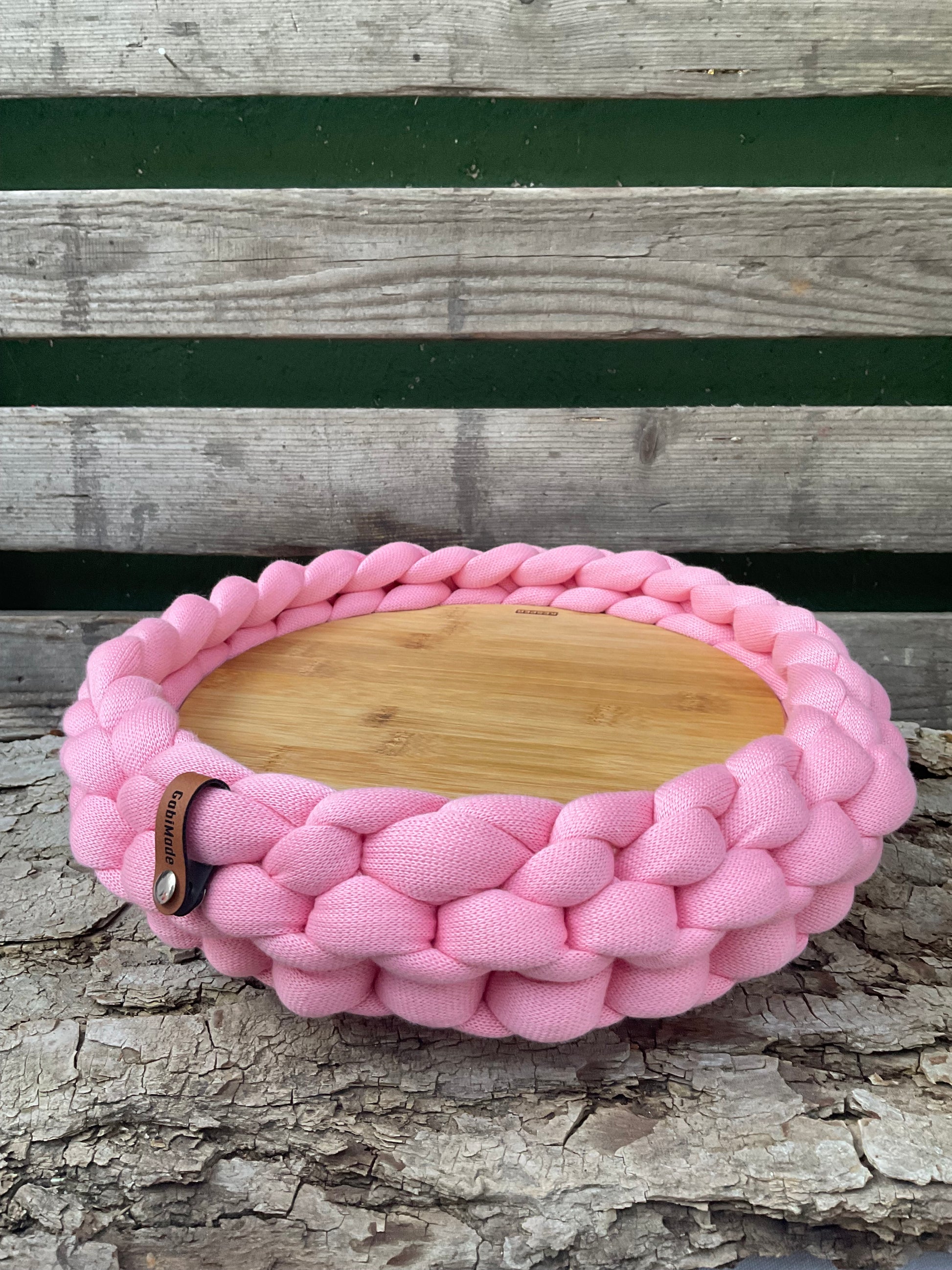 Ein gestricktes Tablett in rosa mit Holzteller 