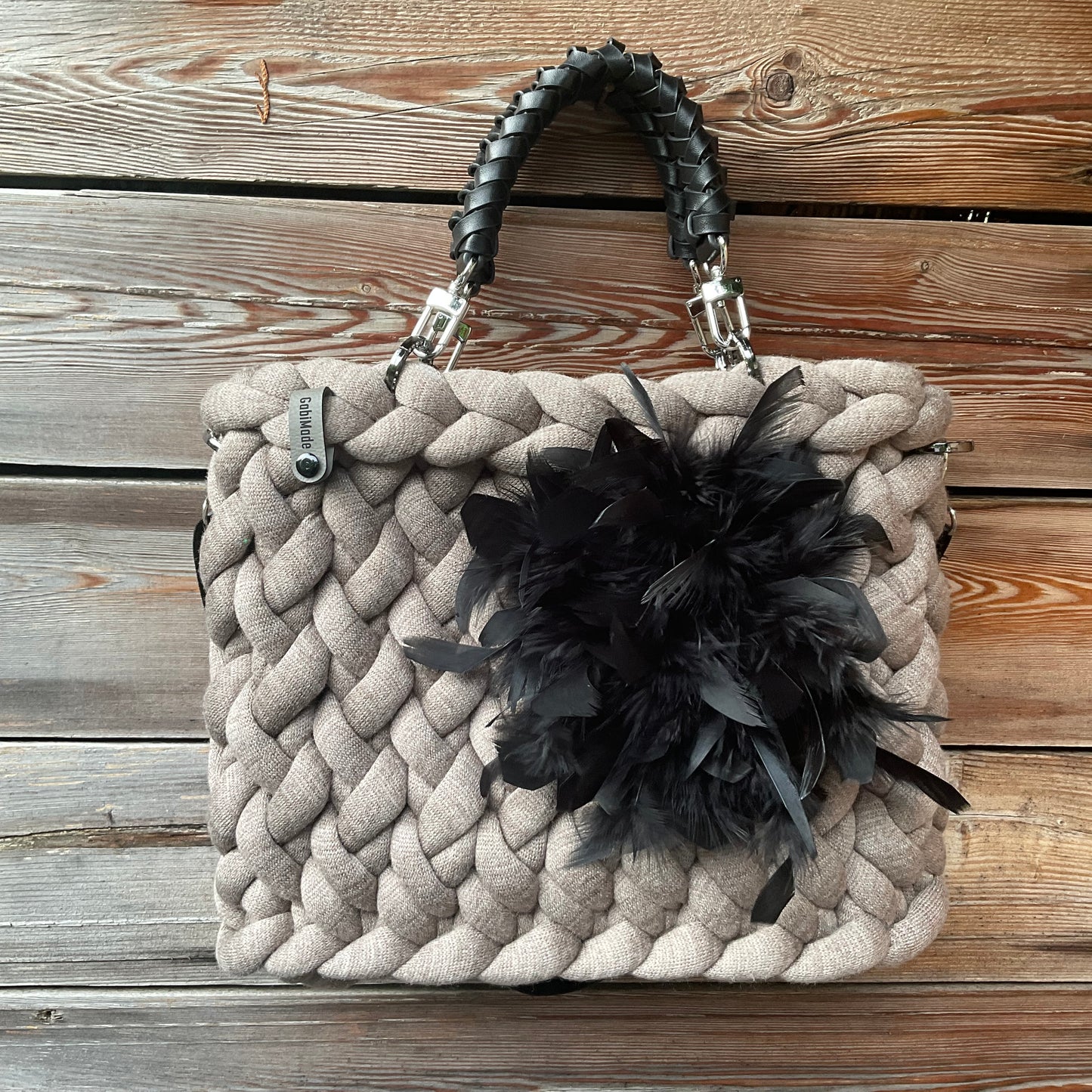 Eine gestrickte Tasche in Taupe mit schwarzen geflochtenen Griffen 