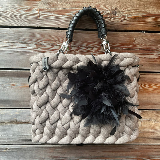 Eine gestrickte Tasche in Taupe mit schwarzen geflochtenen Griffen 