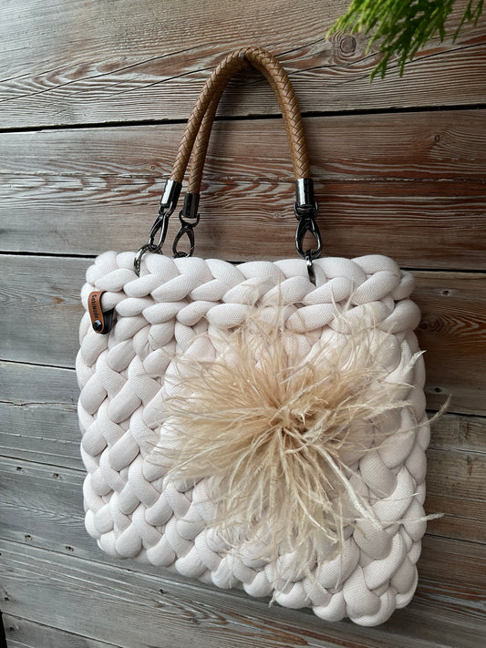Eine gestrickte cremefarbene Tasche mit Federbrosche und Griffen