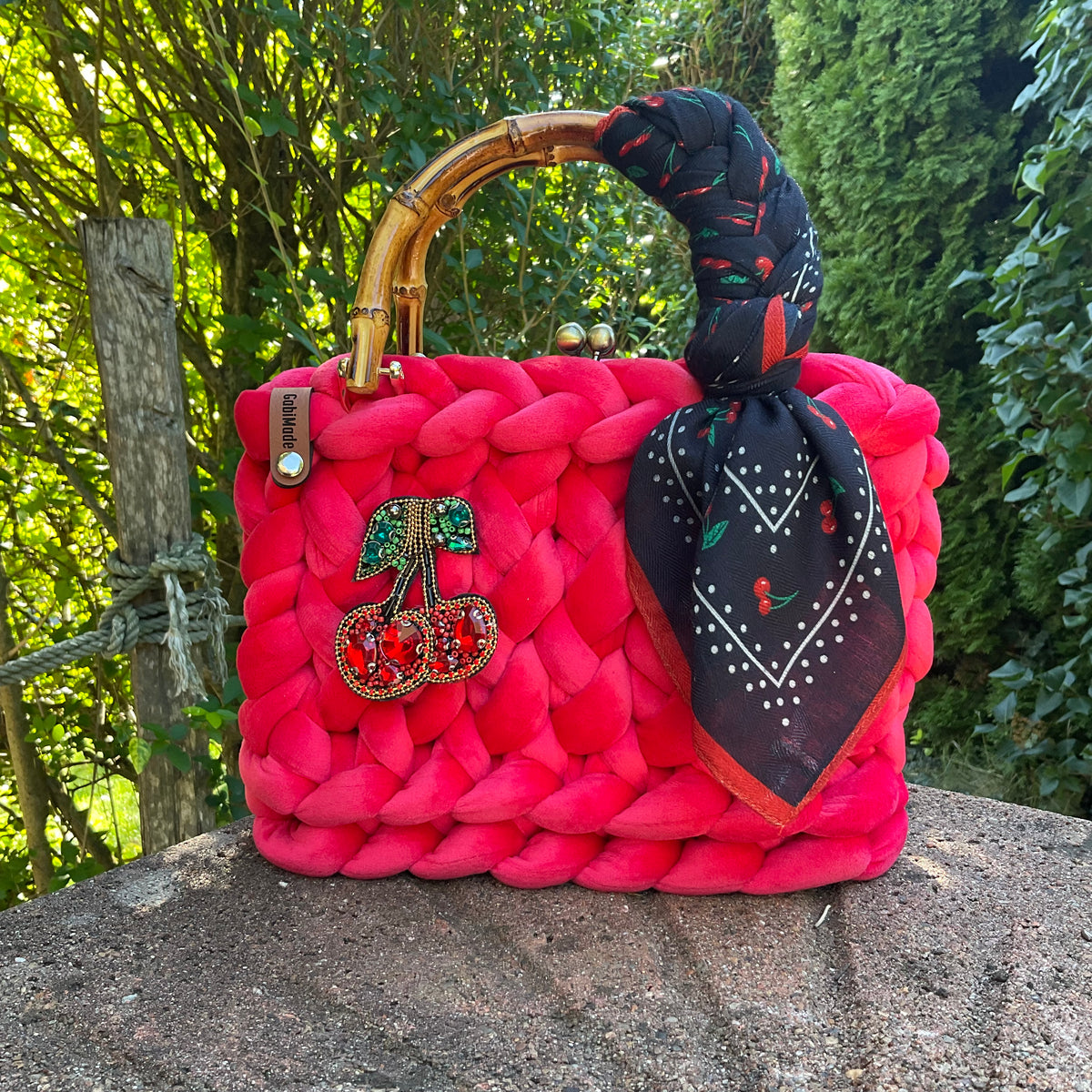 Eine gestrickte kirschrote Trachtentasche mit Brosche und Bambusgriffen 