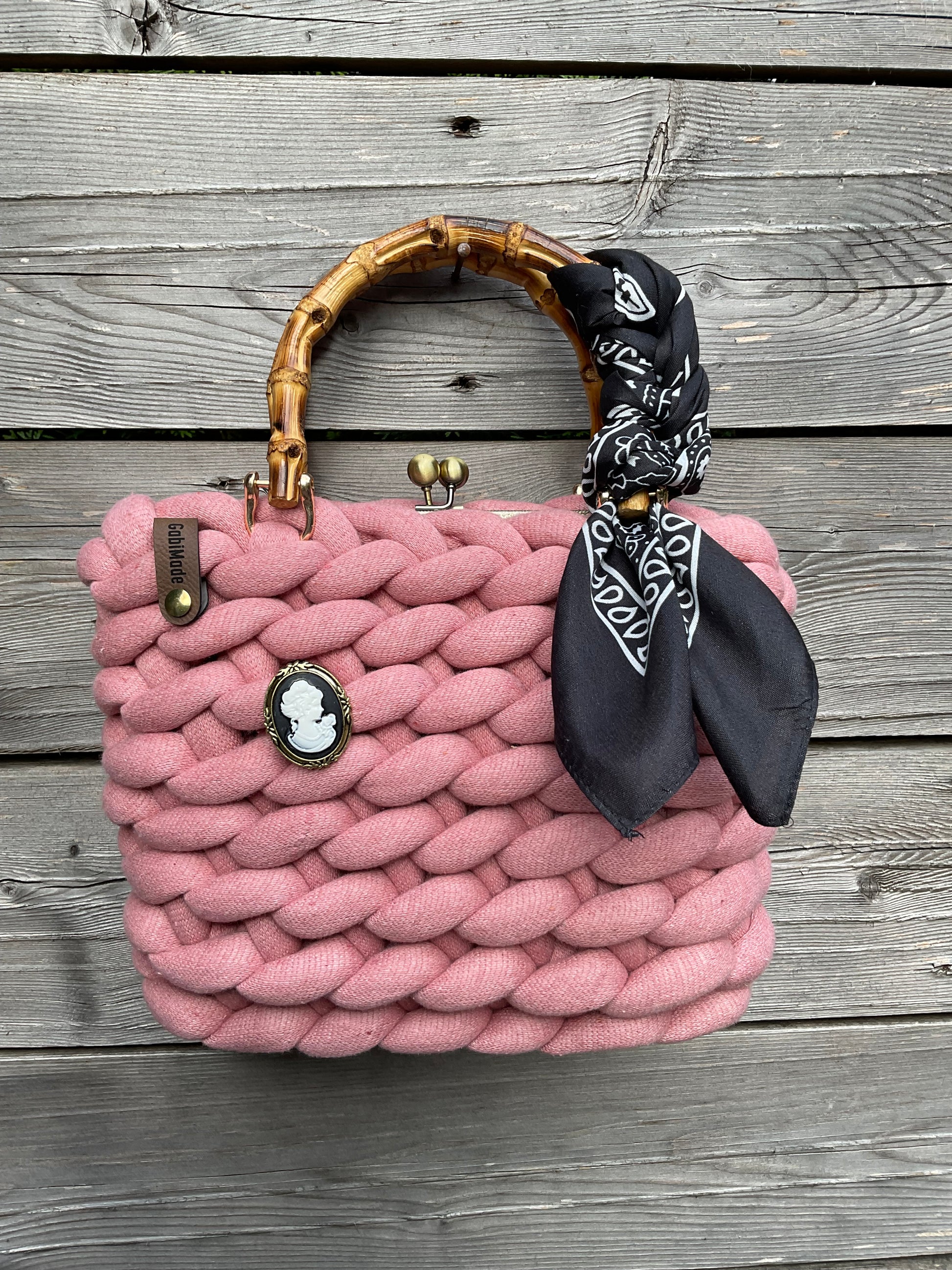 Eine gestrickte rosa Trachtentasche mit einem drapierten Tuch um den Griff und einer Brosche.