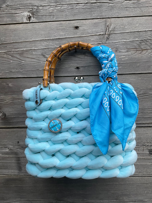 Eine hellblaue gestrickte Trachtentasche mit Tuch und Brosche 