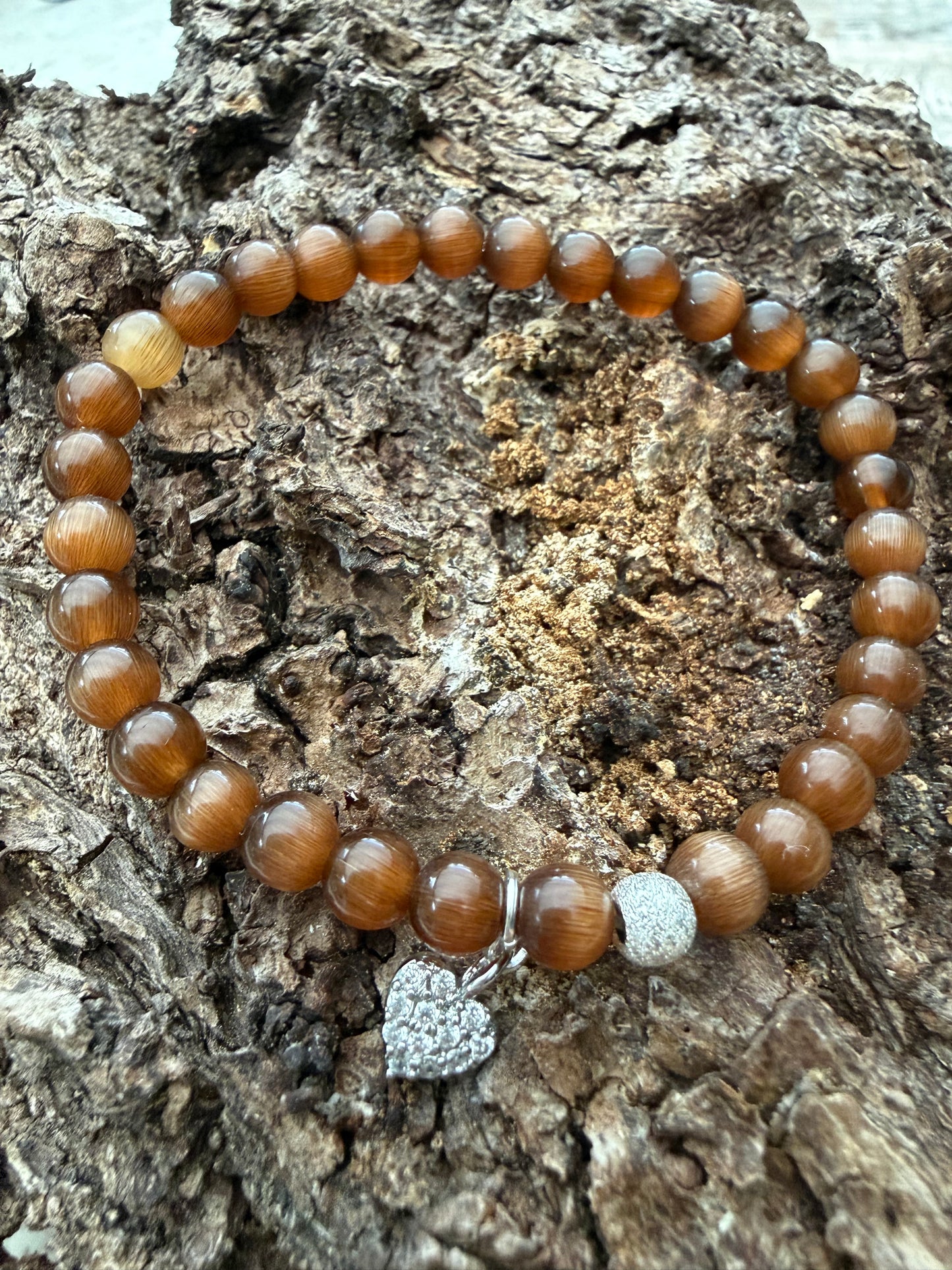 Ein braunes Perlenarmband mit Silberperle und Herzanhänger 