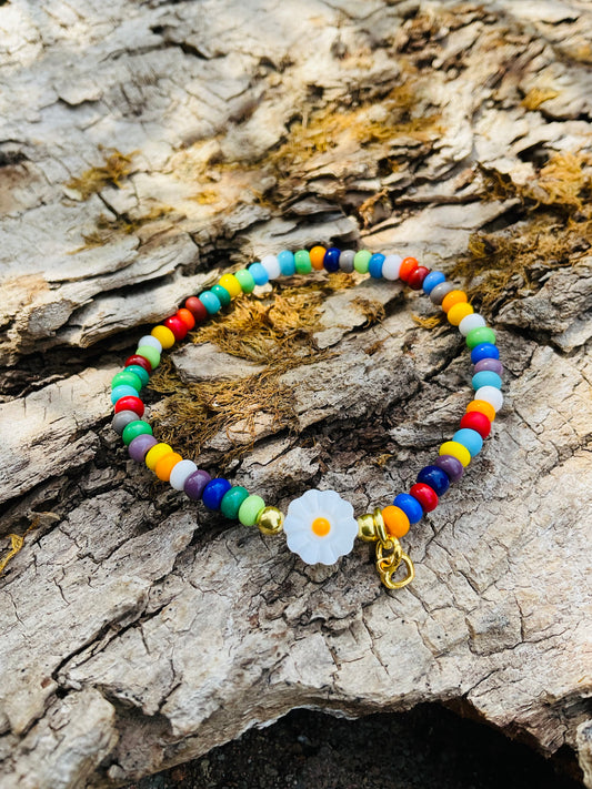 Ein buntes Armband mit einer Blumenperle und einem goldenen Herzanhänger