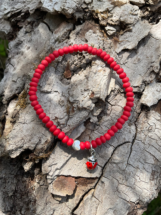 Ein rotes Armband mit einem slbernen Herz und einem Marienkäfer Anhänger