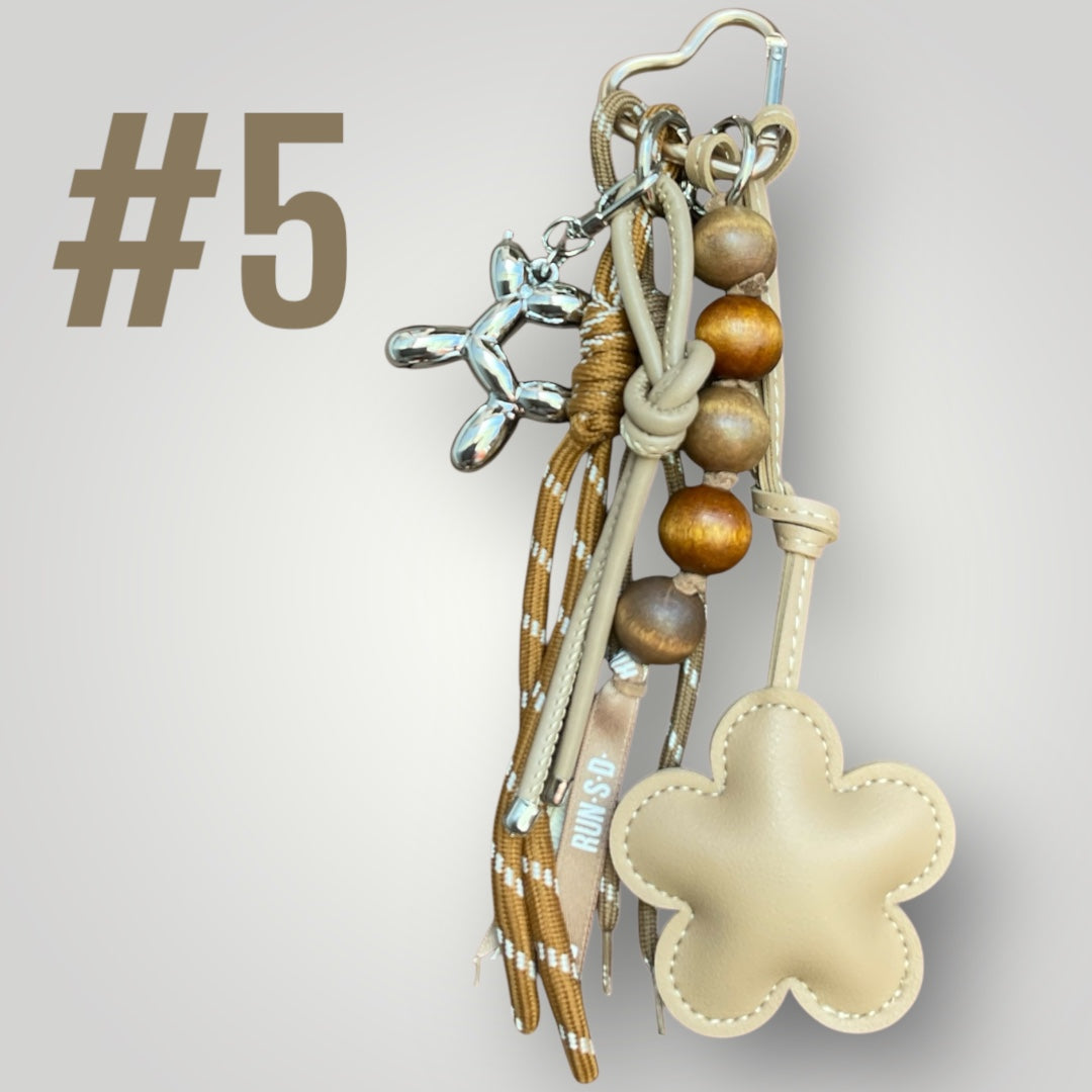 Ein Beige und brauner Taschenanhänger mit einer Blume und einem silbernen Ballonhund