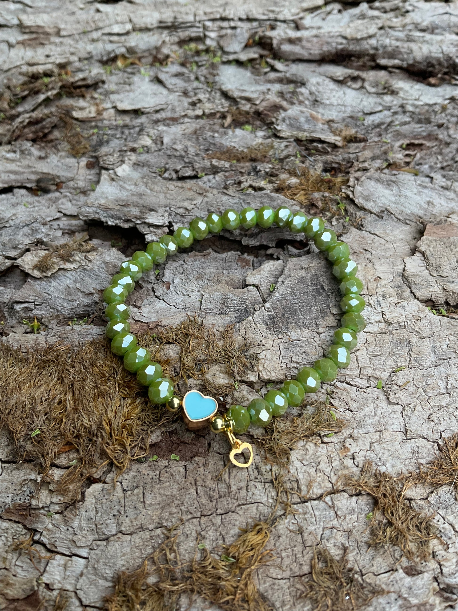 Ein grünes Armband mit einem türkisen Herz und einem goldenen Herzanhönger