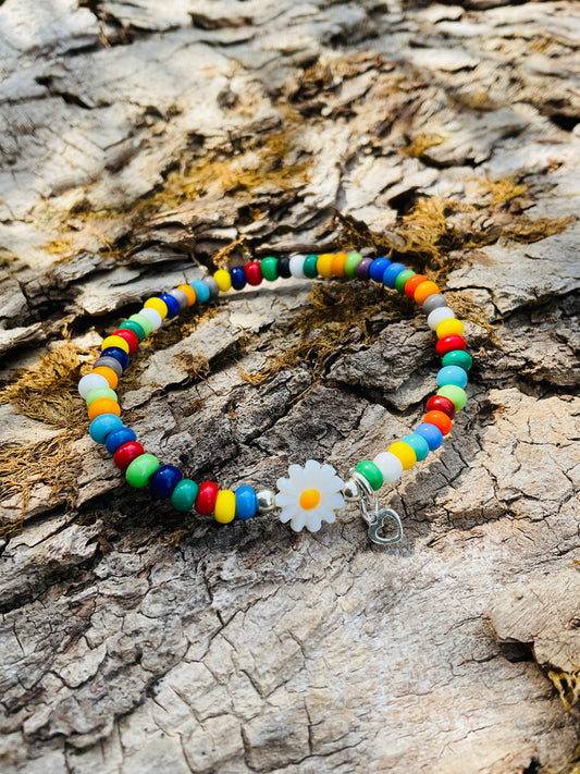 Ein buntes Armband mit einer Blumenperle und einem silbernen Herzanhänger