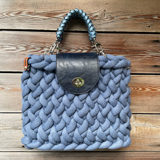 Eine gestrickte blaue taschevmit Klappe und geflochtenen Griffen 