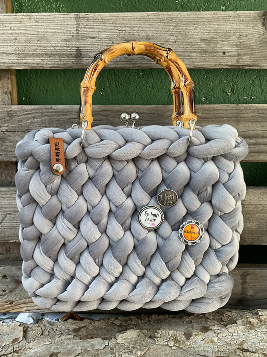 Eine gestrickte graue Tasche mit anstecker und Griffen 